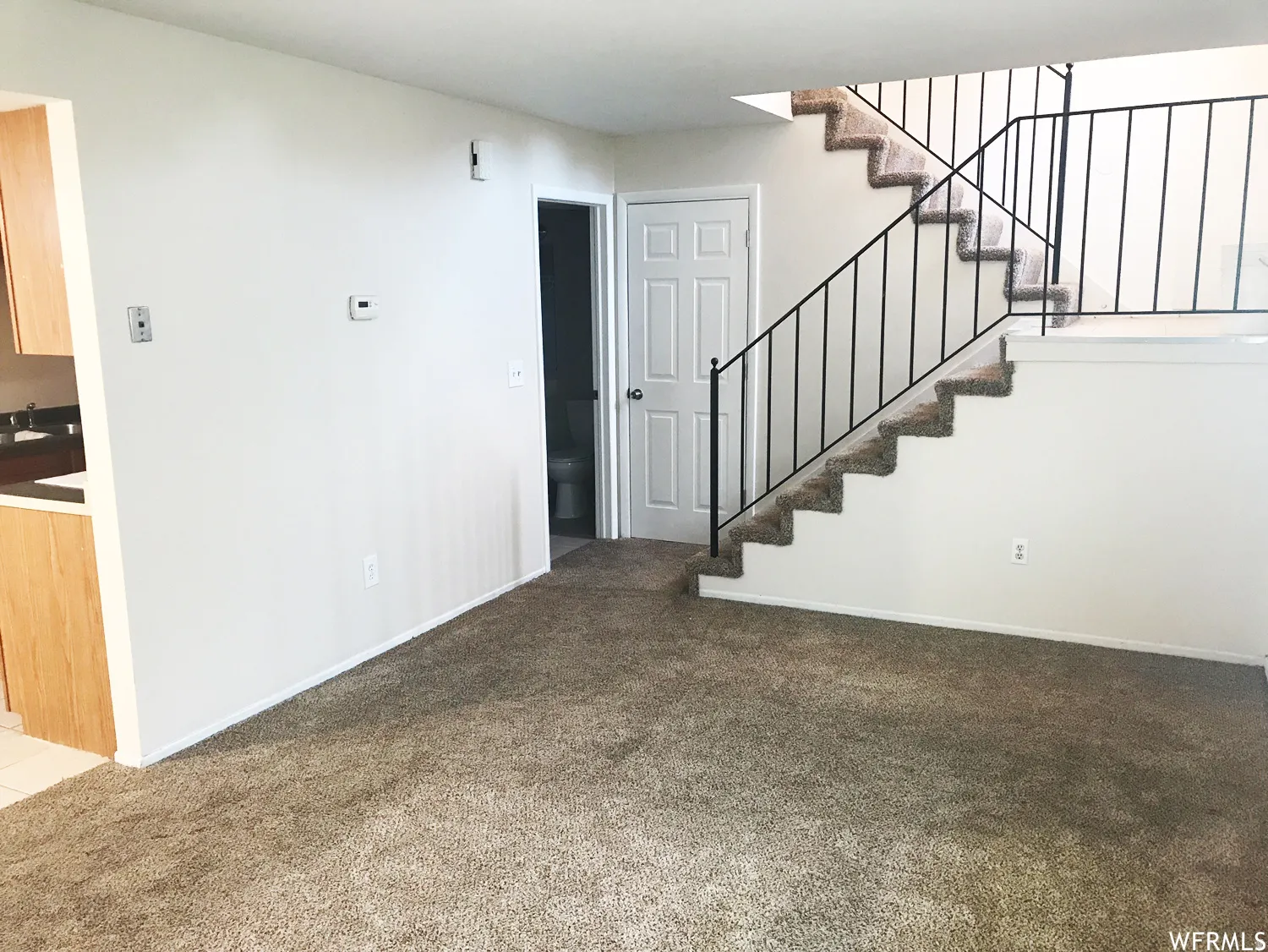 Carpeted living space with a white interior door and a staircase featuring black metal railings