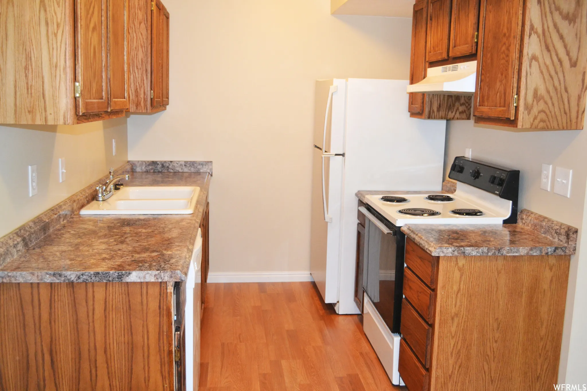 Kitchen featuring wood-finish cabinetry, laminate countertops, a double basin sink with chrome faucet, a white electric range with hood, and a full-size refrigerator