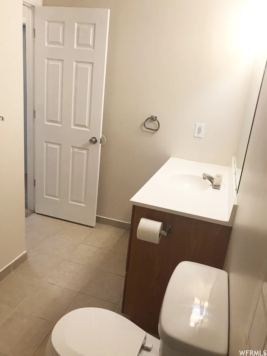 Bathroom featuring a wood-finish vanity with an integrated sink and chrome faucet, a white two-piece toilet, and light-toned tile flooring