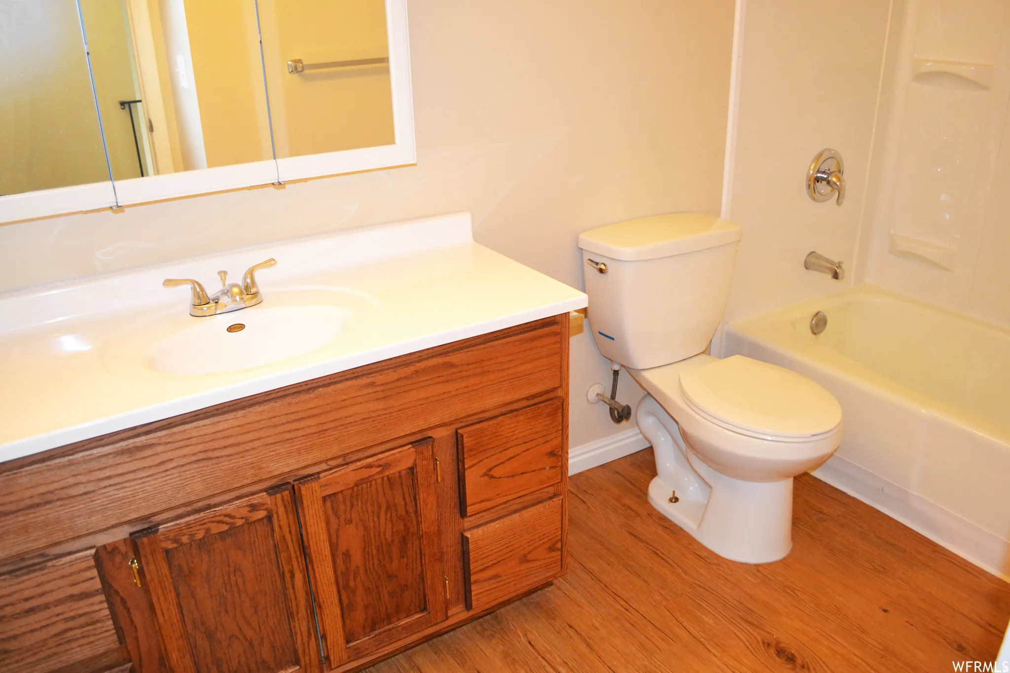 Bathroom featuring a wood-finish vanity with a white countertop and integrated sink, a white toilet, and a white tub with a shower surround