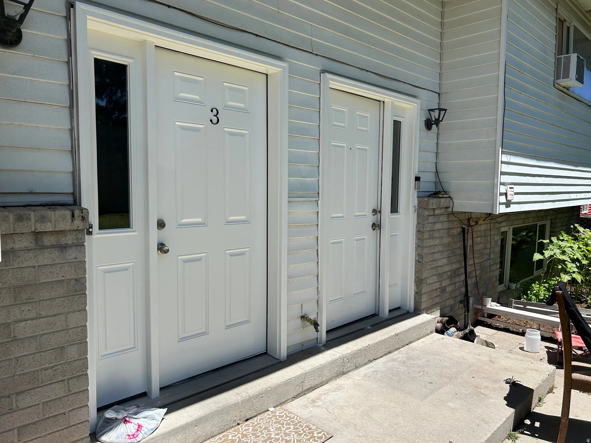 Dual white paneled entry doors with sidelights, complemented by light blue horizontal siding and a brick-finish foundation