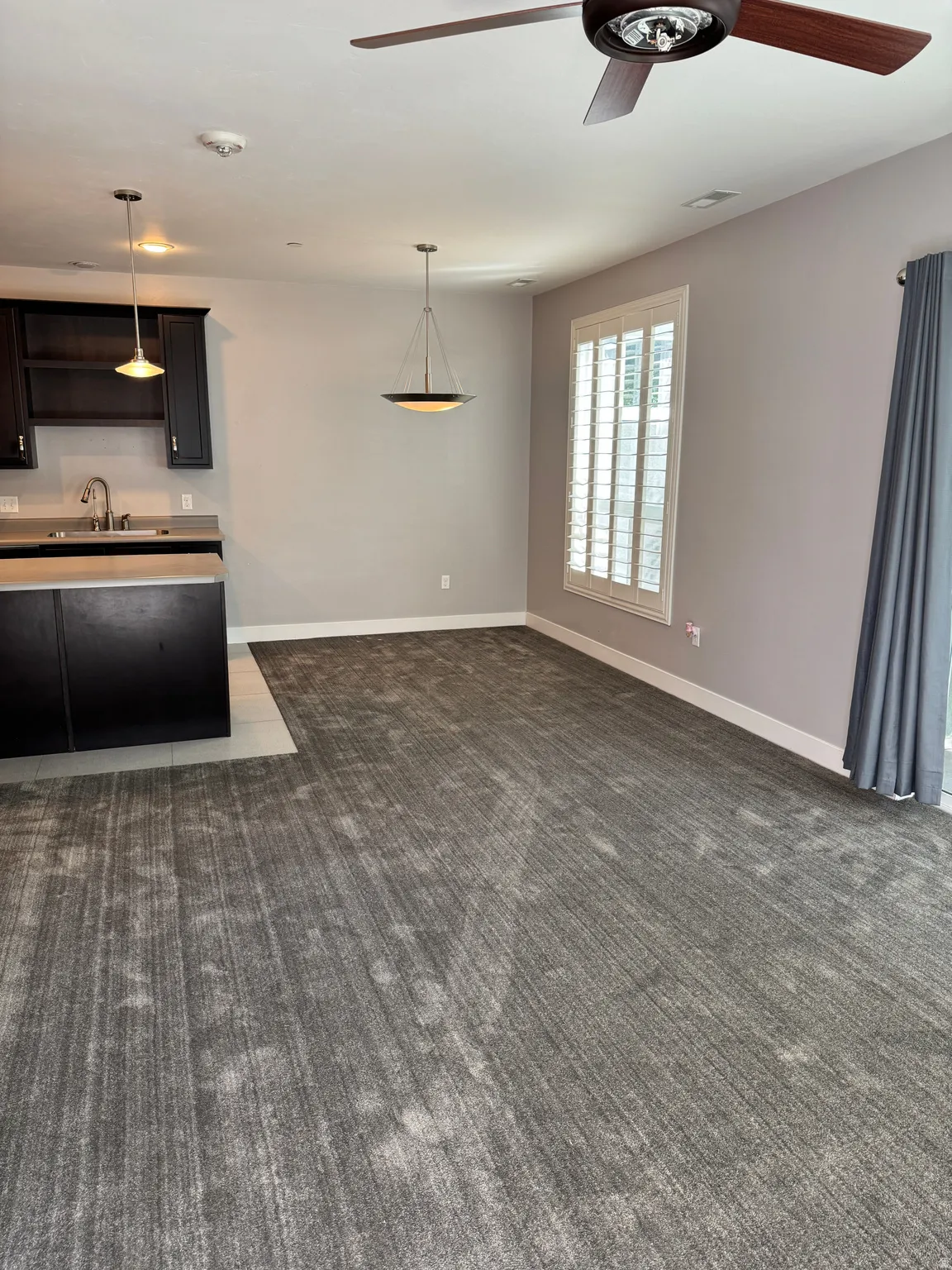 Spacious interior featuring neutral-toned walls, patterned gray carpeting, and a modern ceiling fan
