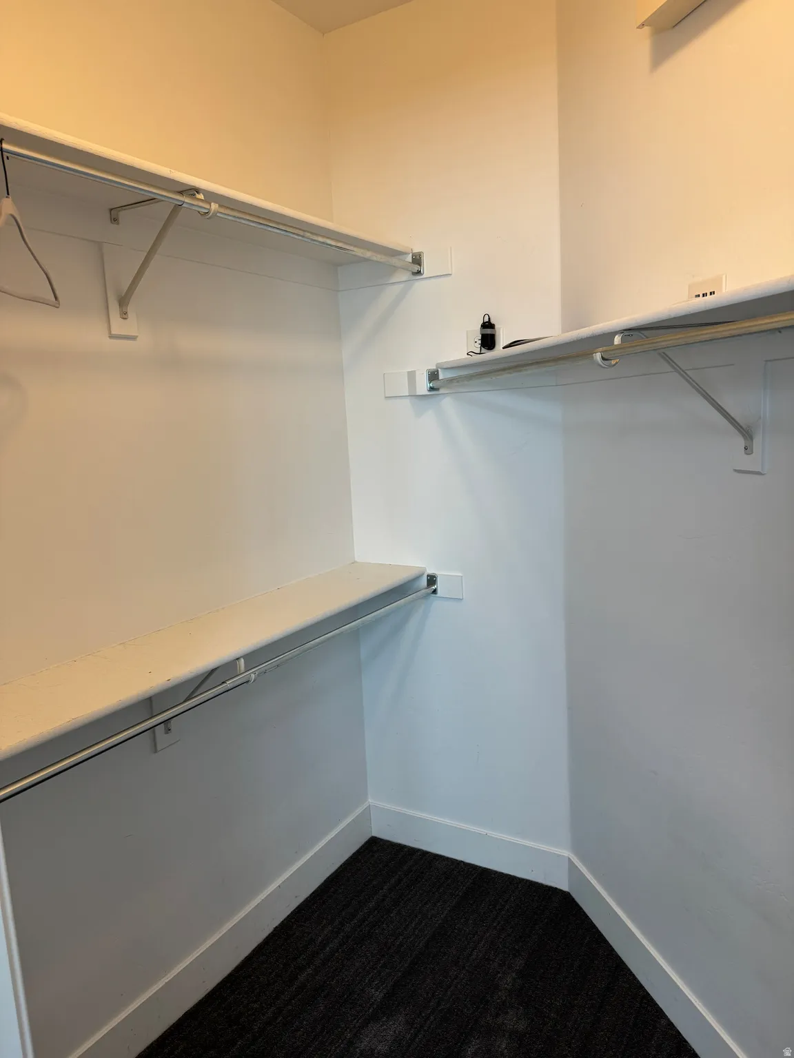 Walk-in closet featuring white painted walls, white shelving, metal hanging rods, and dark gray carpet flooring