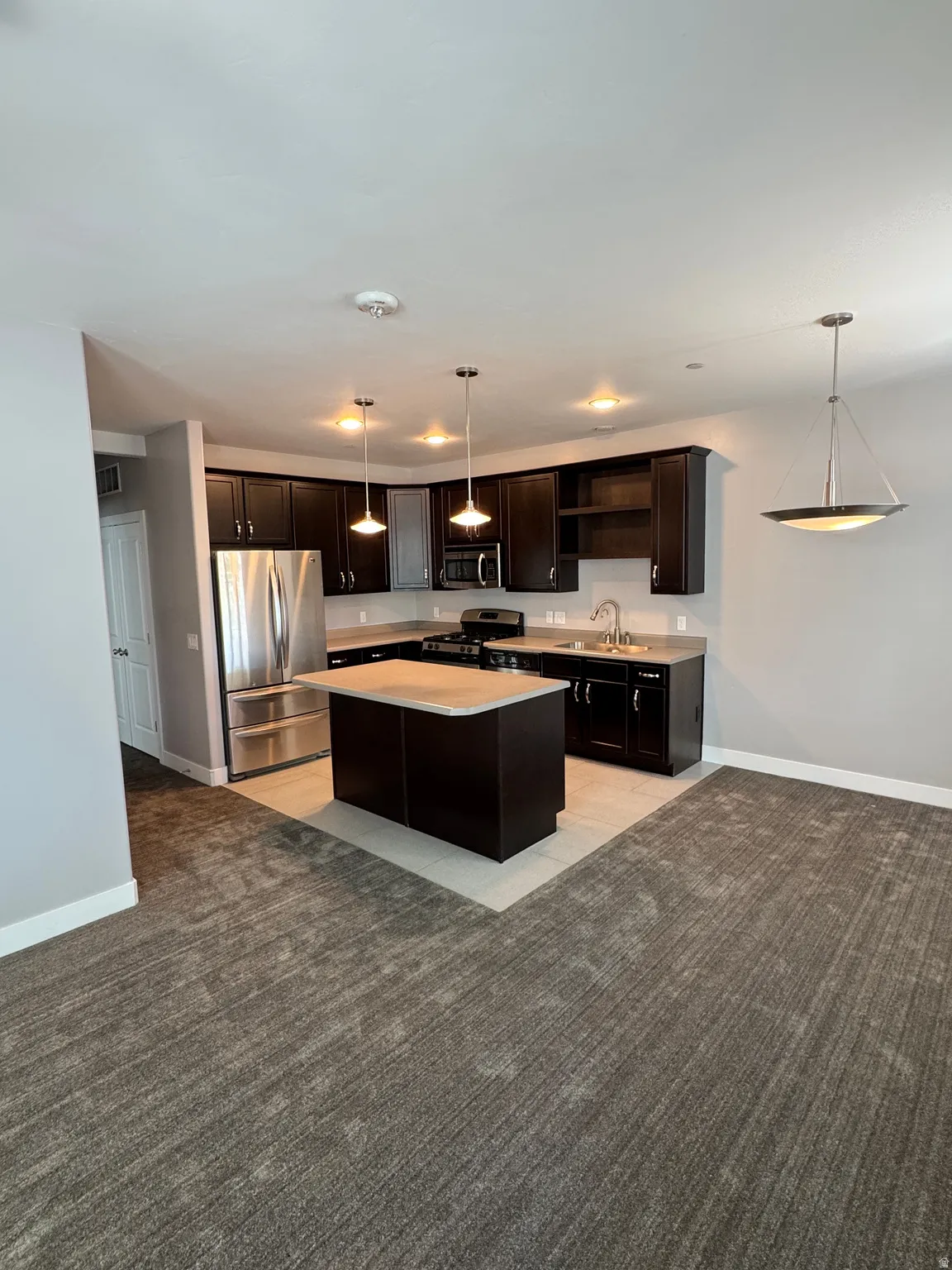 Open-concept kitchen featuring dark wood cabinetry, stainless steel appliances, a center island with a light-toned countertop, and recessed lighting