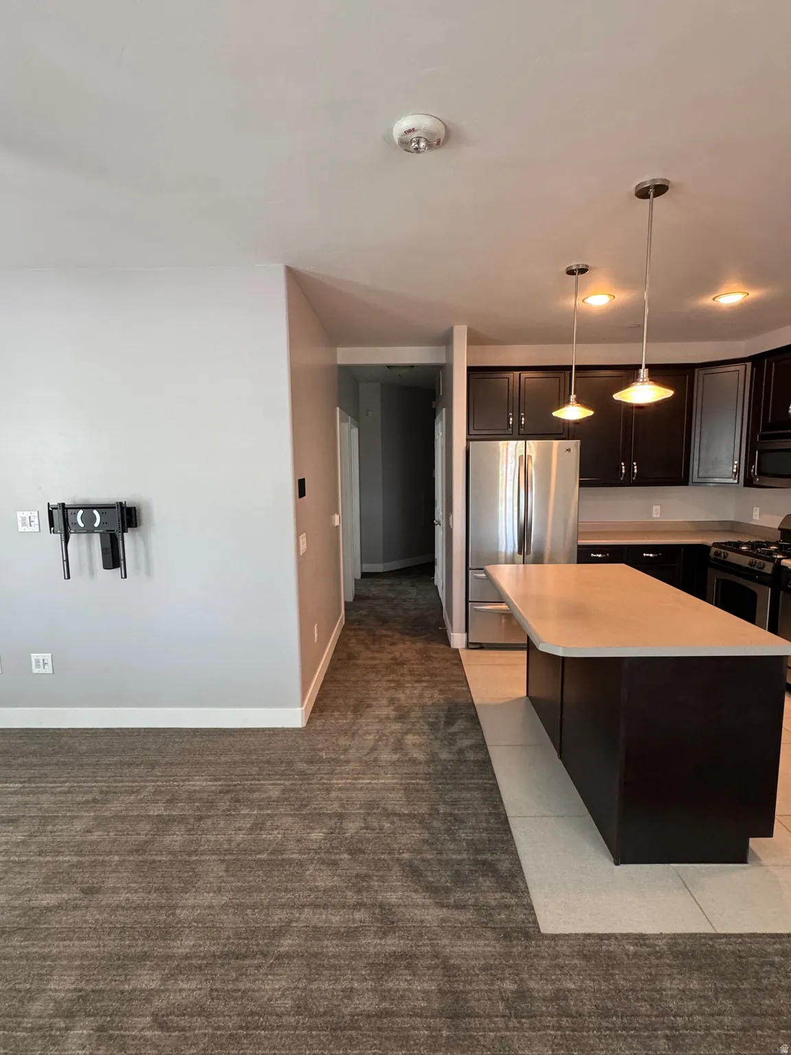 Kitchen featuring dark wood cabinetry, stainless steel appliances, and a central island with a light-toned countertop
