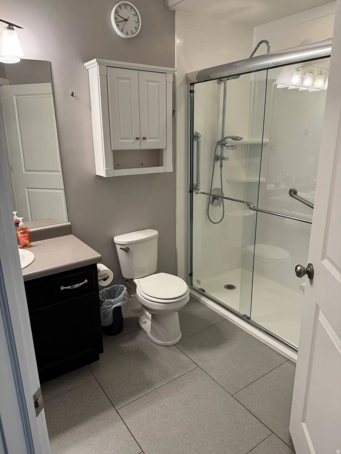 Bathroom featuring a glass-enclosed shower with grab bars, a white toilet, and a vanity with a dark wood-finish cabinet and light-toned countertop