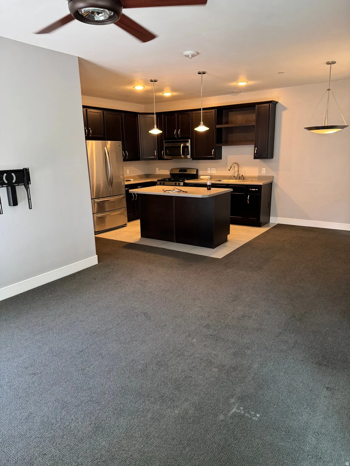 Open-concept kitchen featuring dark wood cabinetry, stainless steel appliances, a central island, and pendant lighting