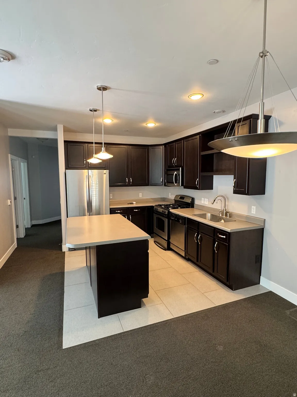 Open-concept kitchen featuring dark wood cabinetry, stainless steel appliances, and a central island with a light-toned countertop