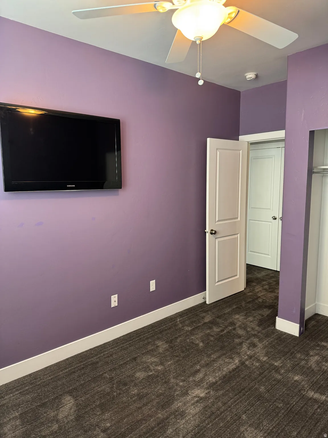 Carpeted room with a ceiling fan light fixture, light purple walls, and white trim