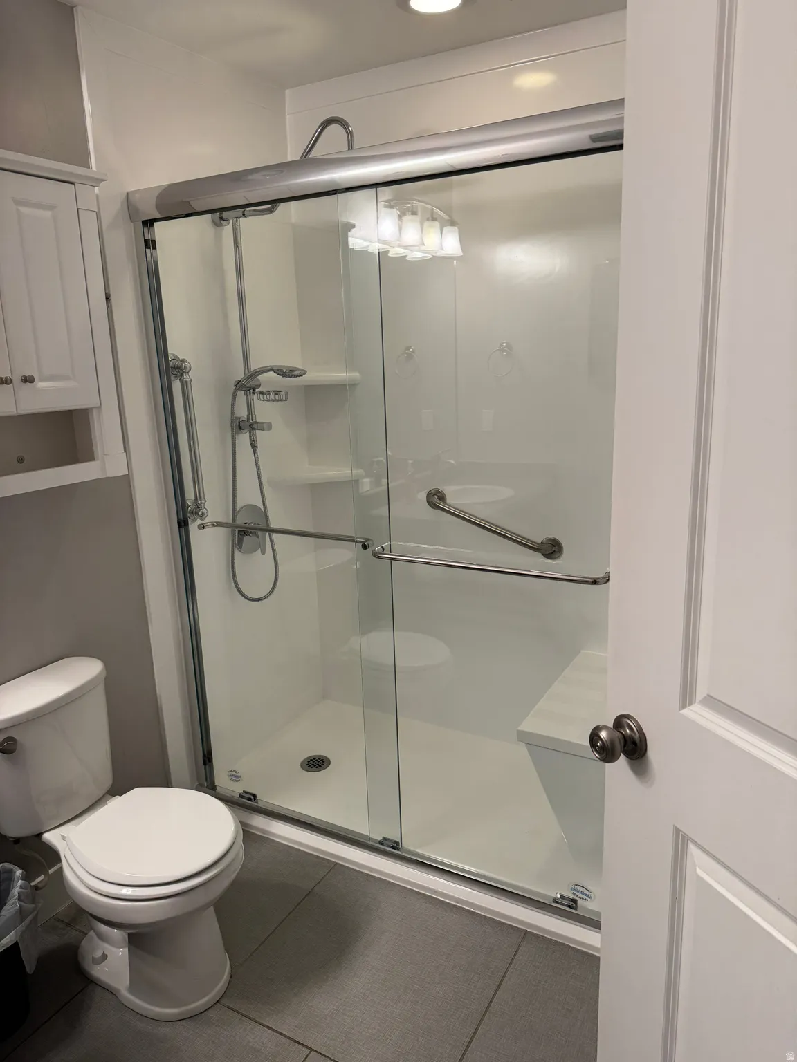 Walk-in shower with sliding glass doors, built-in bench, shower wand, and grab bars