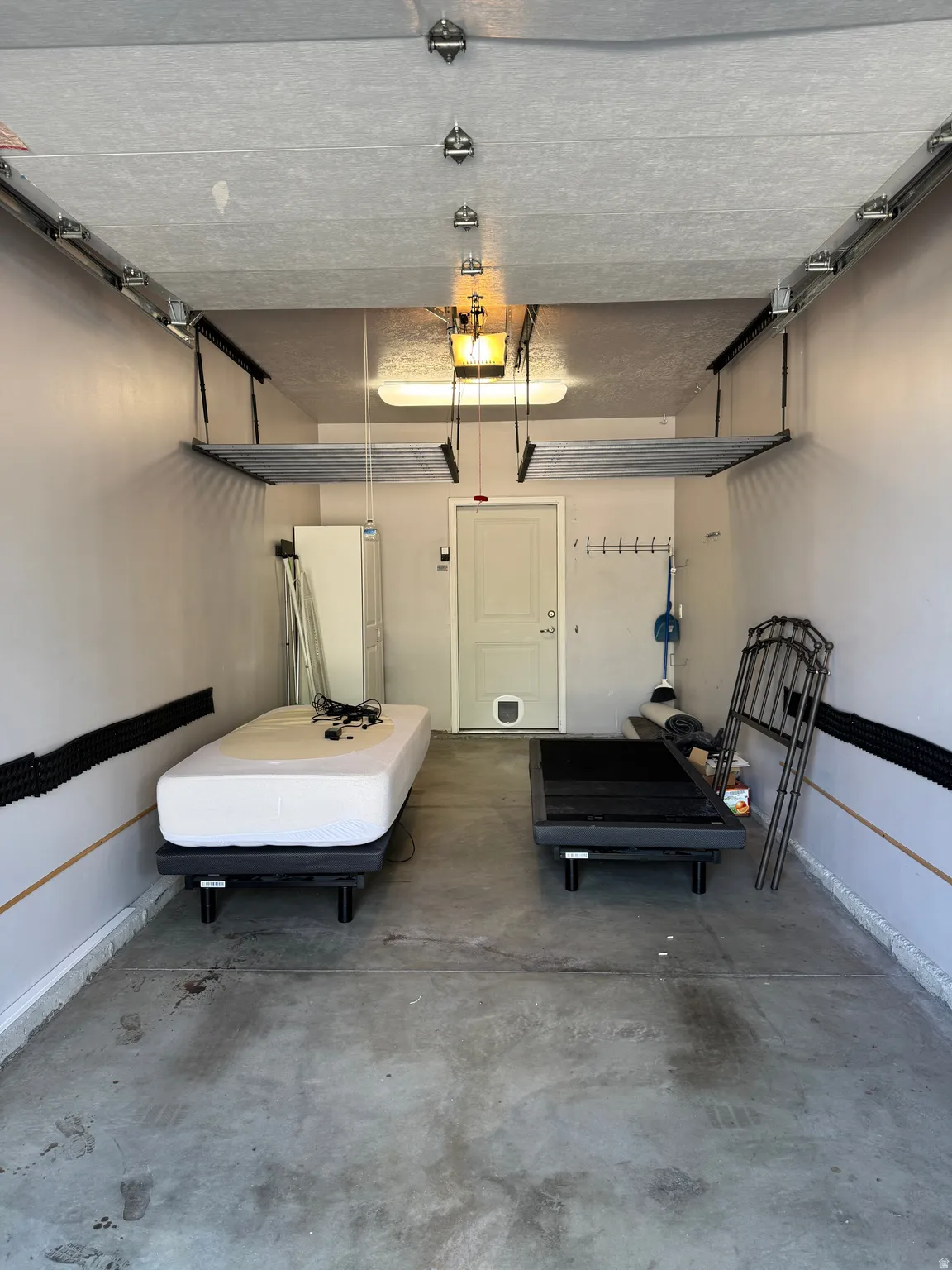 Concrete flooring garage featuring overhead storage shelves, built-in wall hooks, and an attached door with a pet door insert