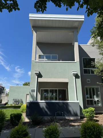 Modern multi-story exterior with a cantilevered balcony, stucco siding, and a street number plaque