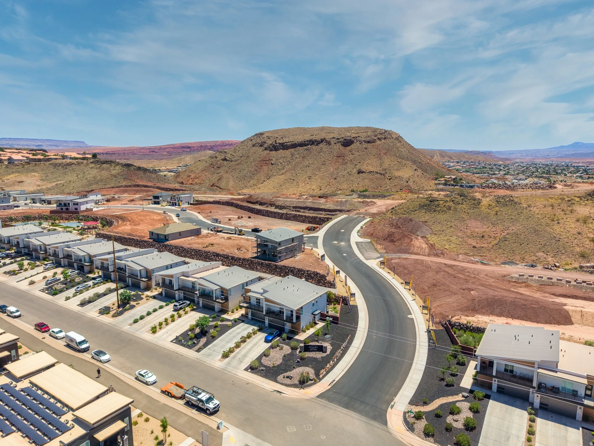 Modern residential development featuring a row of multi-story homes with flat roofs and balconies, set against a desert landscape with prominent rock formations