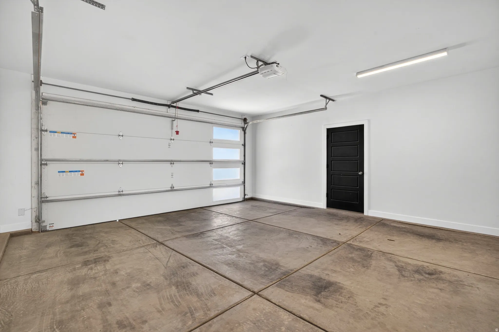 Spacious garage with a white sectional door featuring horizontal window panels, a side entry door with a multi-panel design in black, and concrete flooring