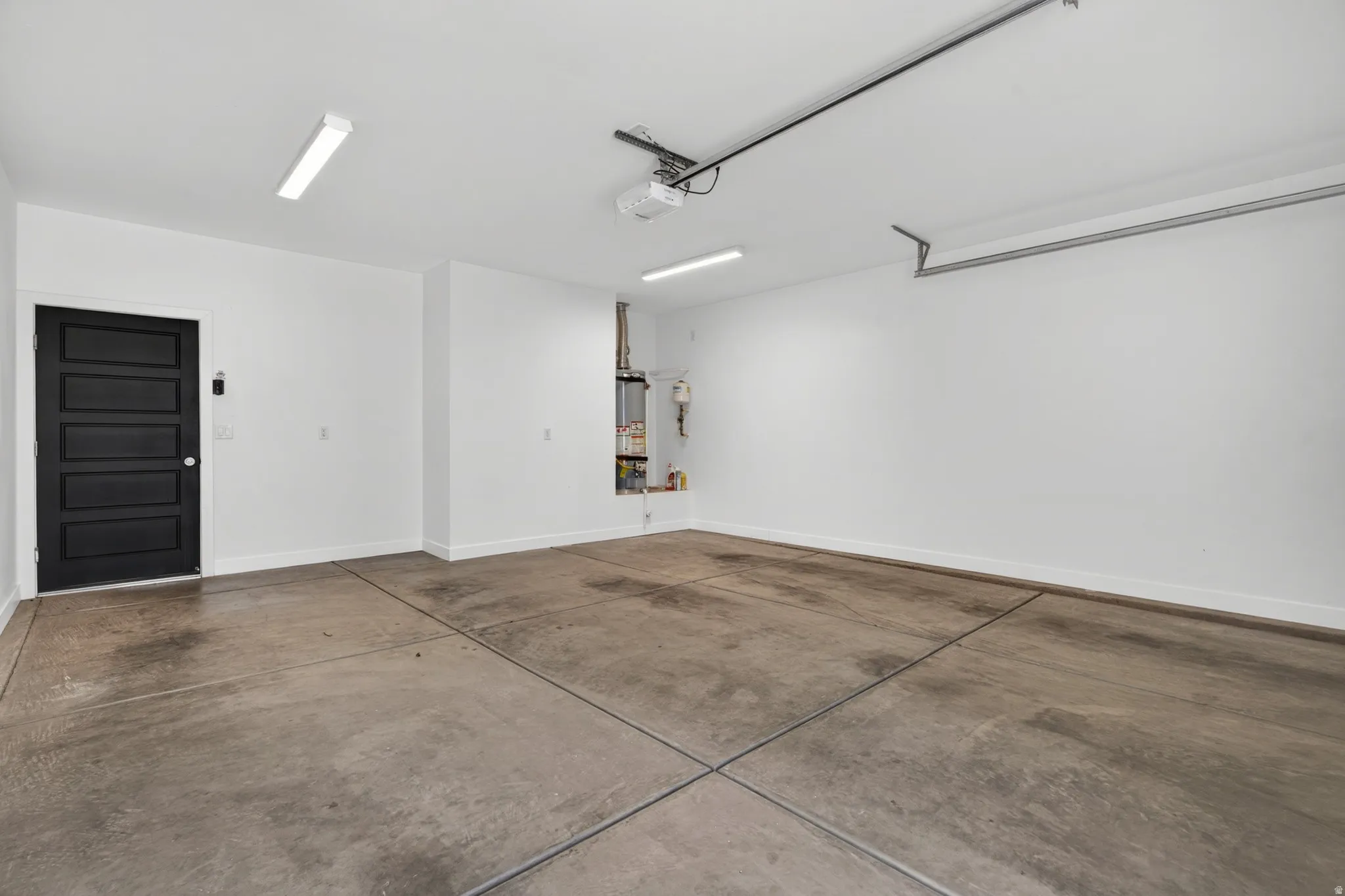 Spacious garage featuring concrete flooring, bright overhead lighting, a dark paneled service door, and painted white walls