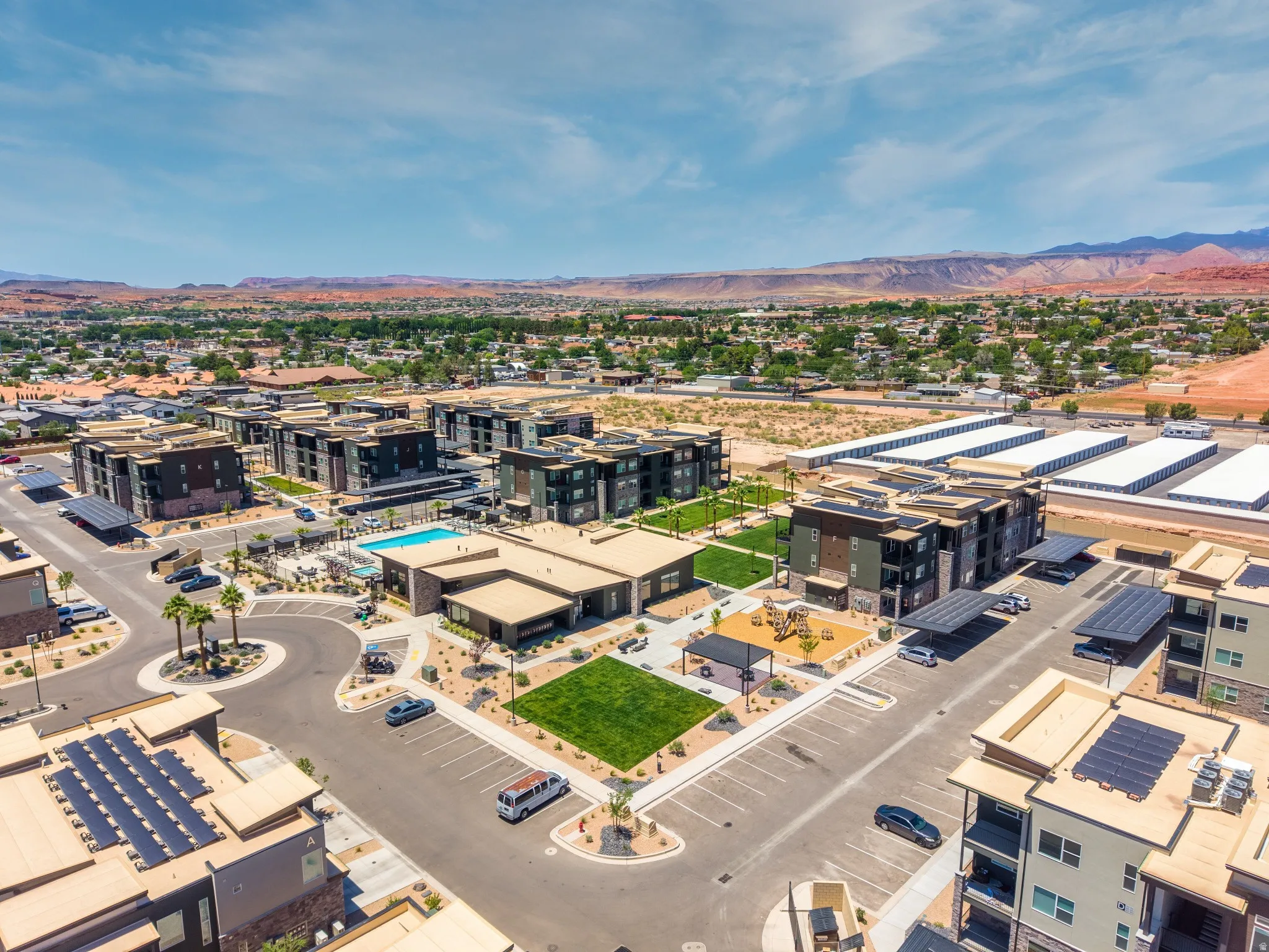 Modern multi-building complex featuring an outdoor swimming pool, paved parking areas, and green spaces