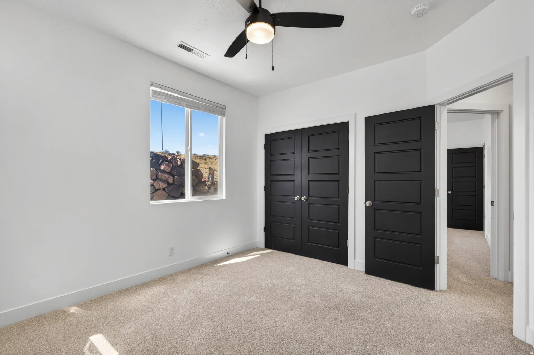 Carpeted room featuring a ceiling fan, a window with horizontal blinds, and a built-in closet with matte black paneled doors
