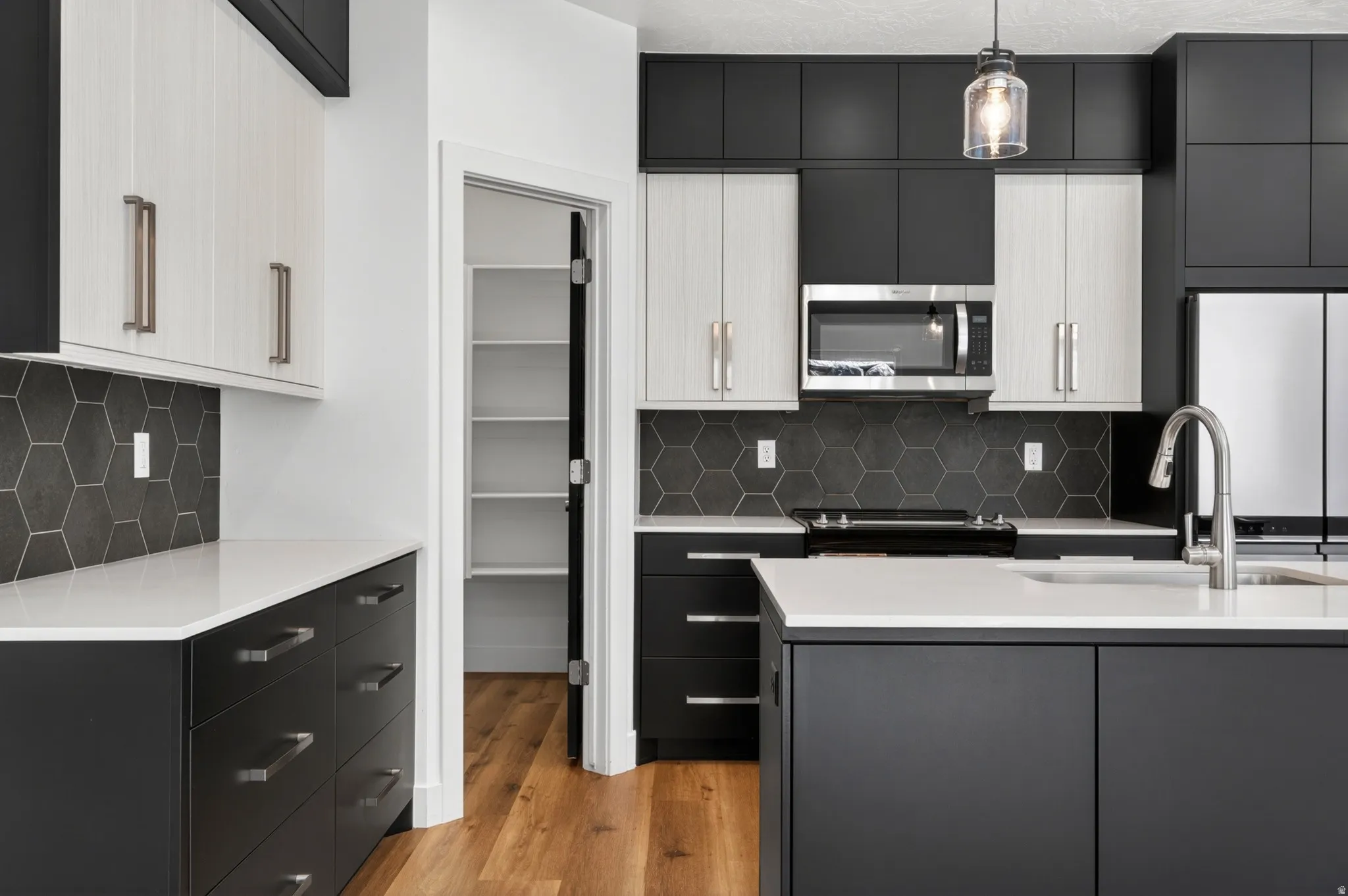 Modern kitchen featuring two-tone cabinetry, stainless steel appliances, hexagon tile backsplash, light countertops, and wood-finish flooring