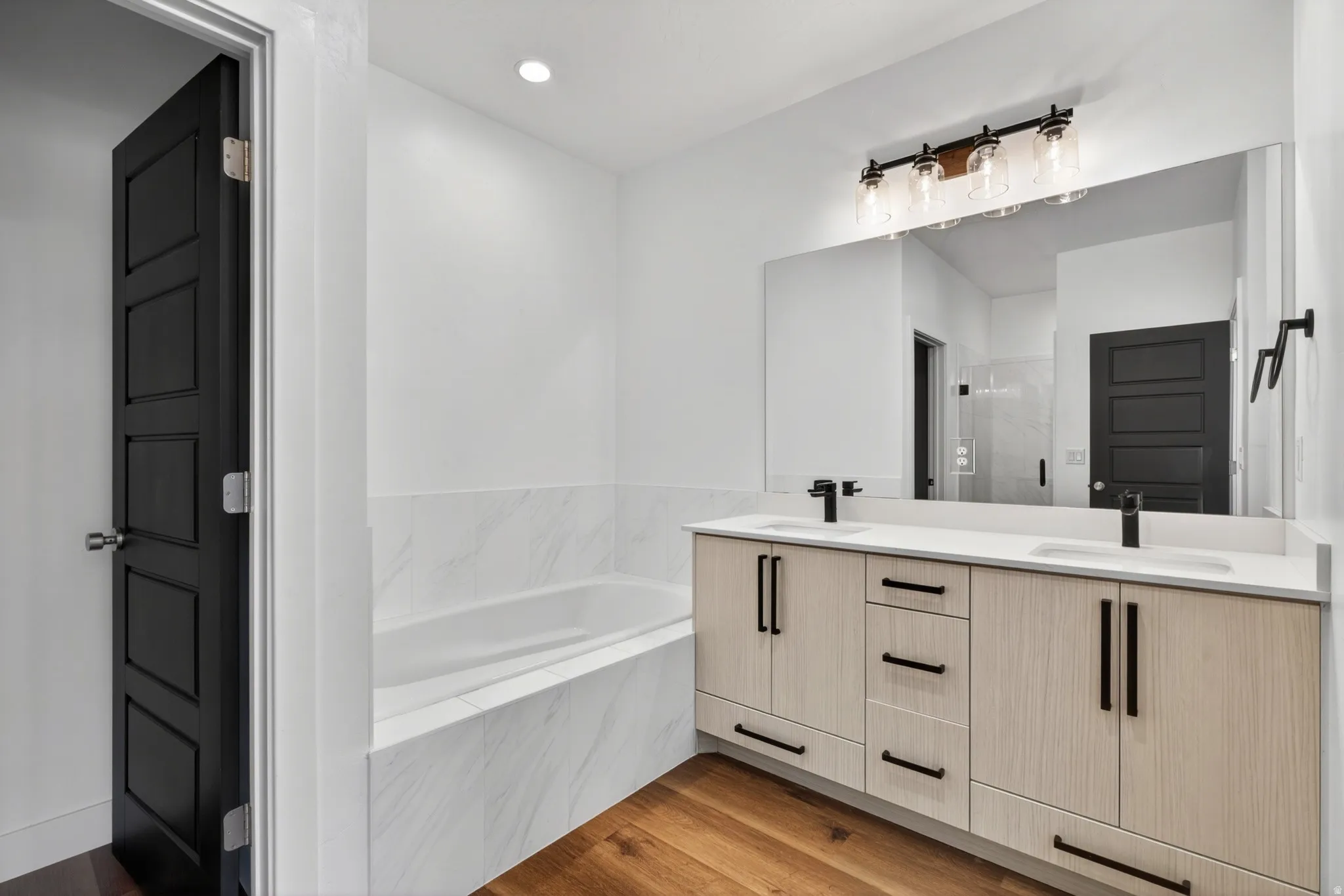 Bathroom featuring a dual vanity with light wood-finish cabinetry, quartz countertops, and matte black fixtures