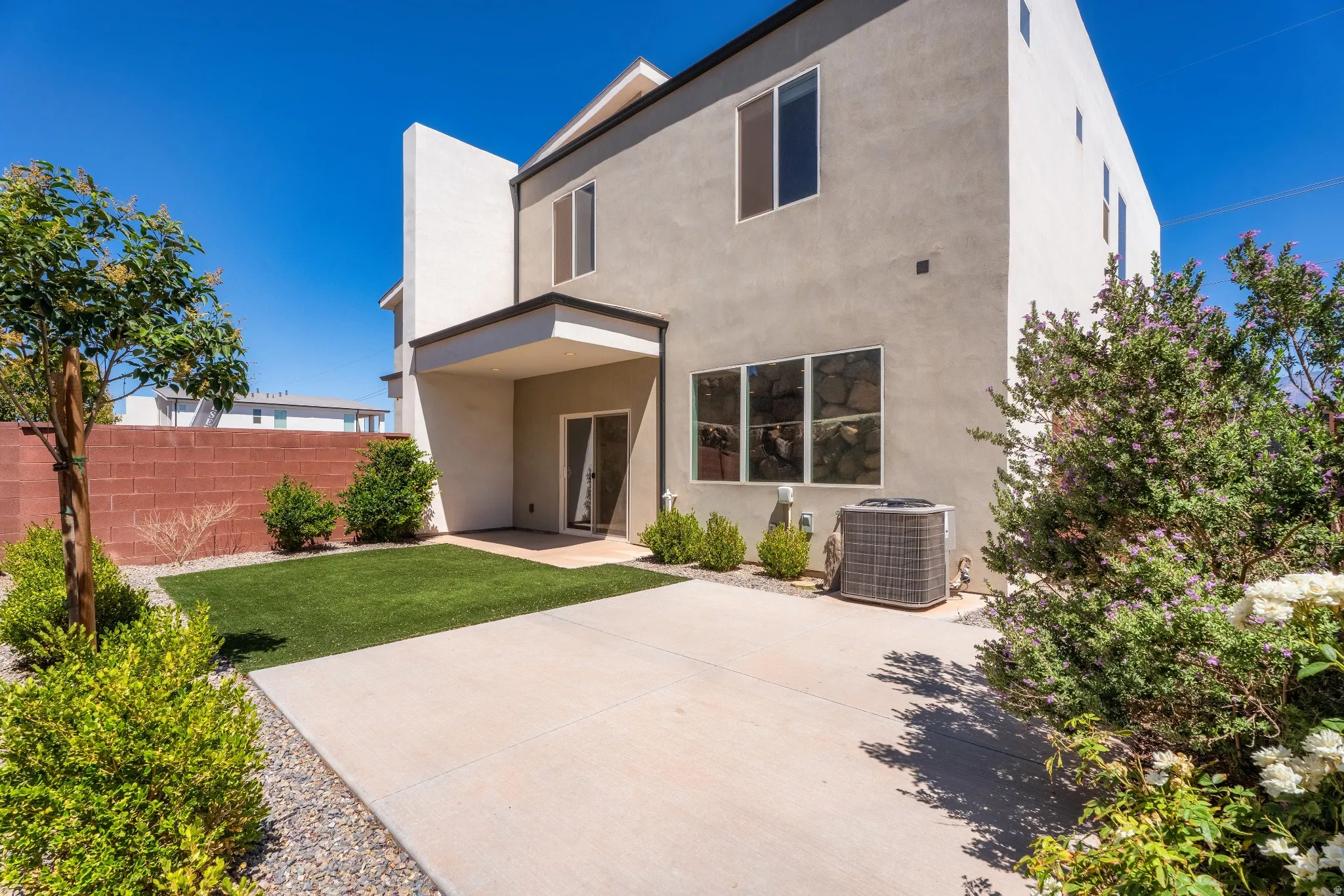 Contemporary exterior featuring stucco siding, multiple windows, and a shaded patio area