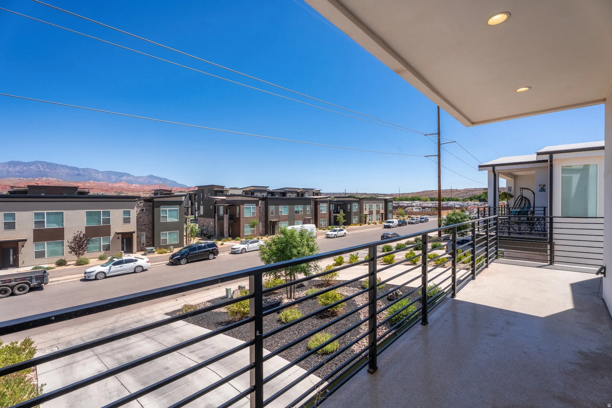 Private balcony with black horizontal bar railing, offering views of the surrounding neighborhood and distant mountains