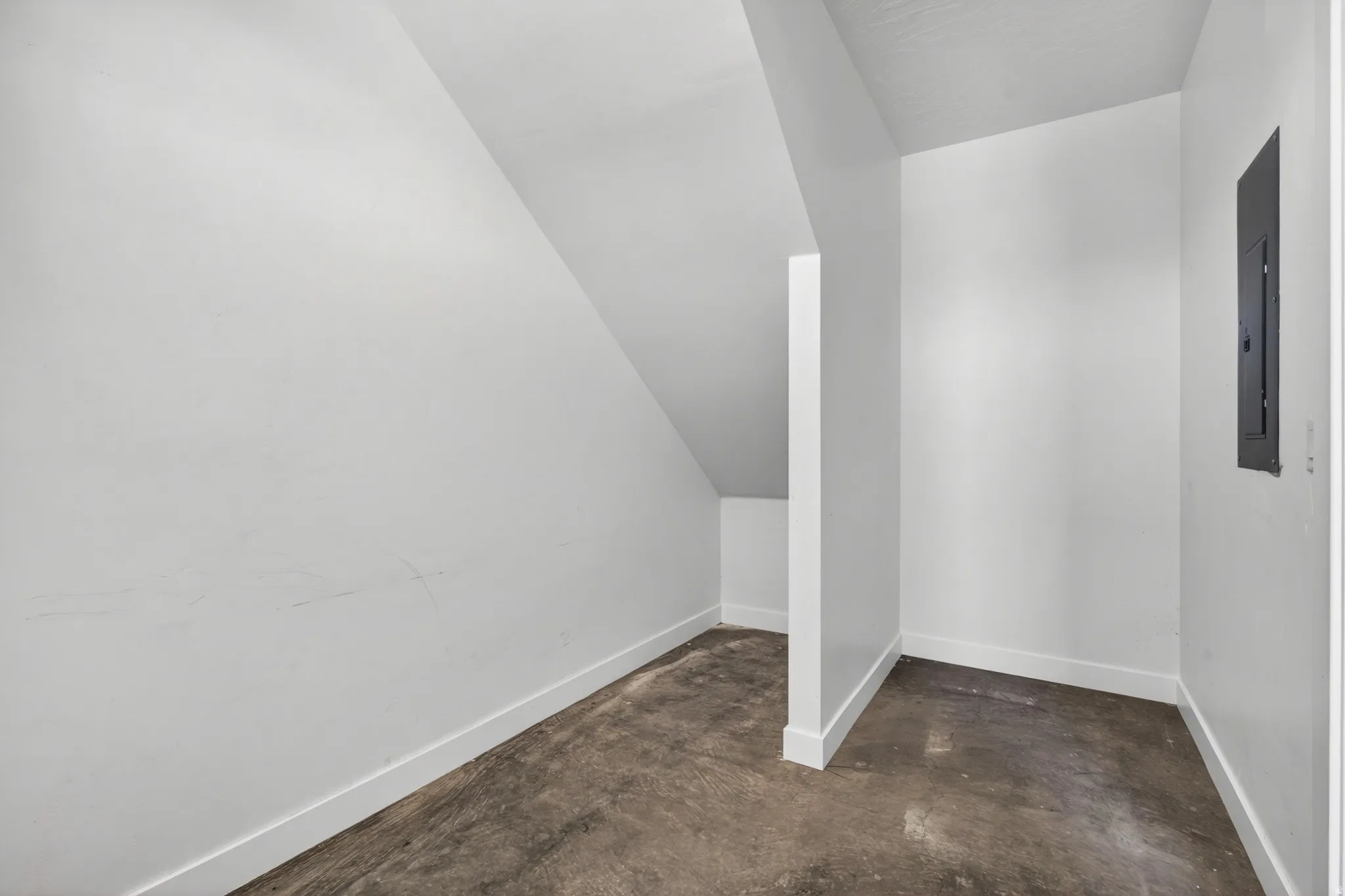 Interior storage area featuring a concrete floor, white walls, and a built-in electrical panel