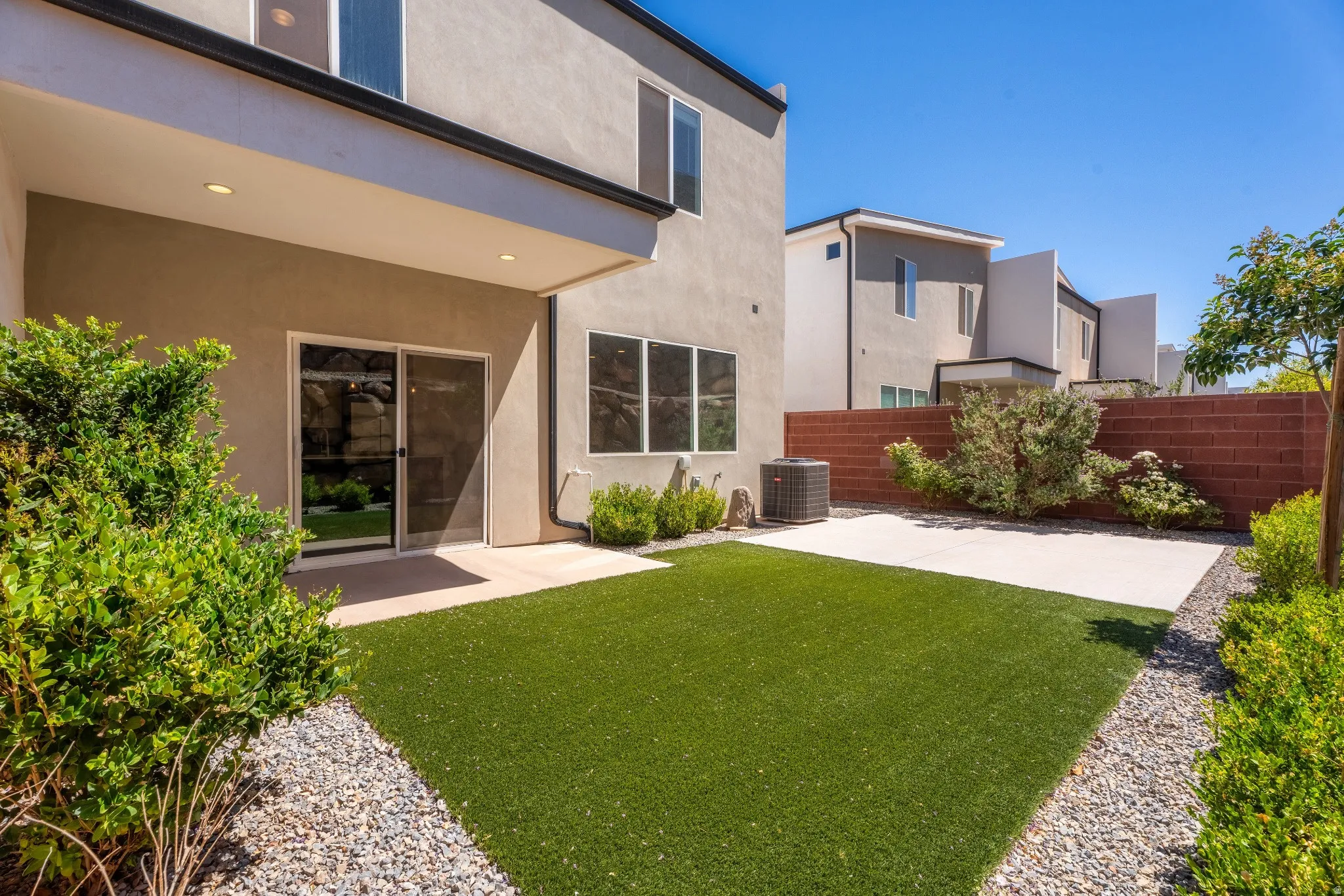 Private backyard featuring artificial turf, a concrete patio, and a red brick privacy wall