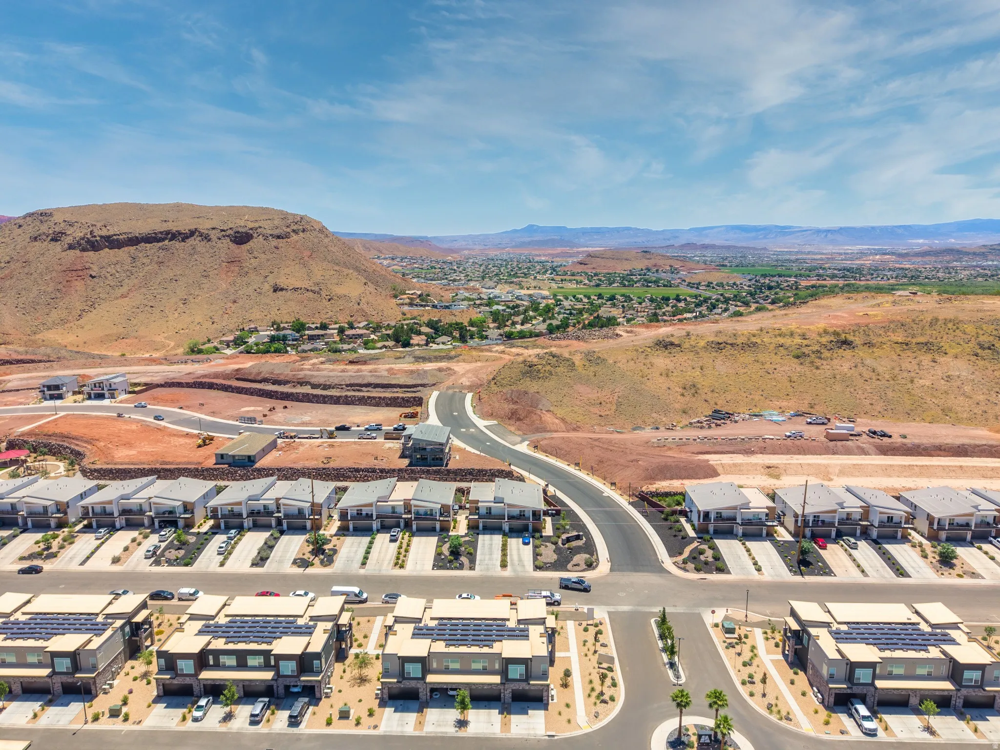 New construction residential development featuring modern architecture, solar panel installations, xeriscaped front yards, paved roadways, and a prominent mountain backdrop