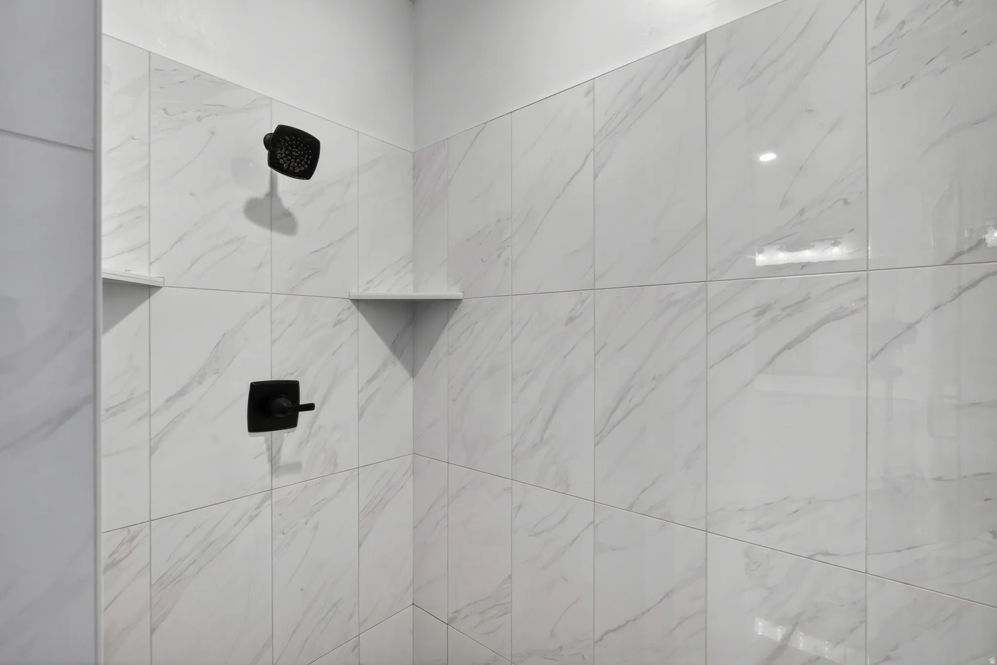 Shower stall featuring large format white tiled walls with subtle veining, matte black showerhead, and matching control handle