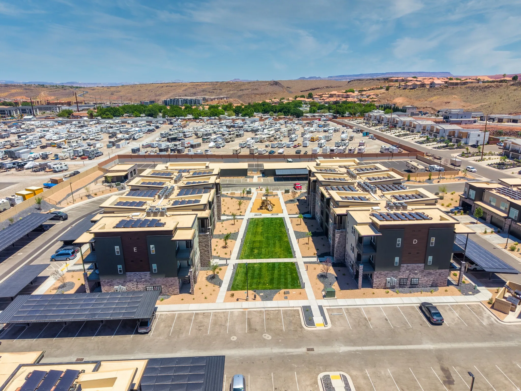 Modern multi-story buildings featuring solar panel installations on rooftops and carports, surrounding a central green space with pedestrian pathways