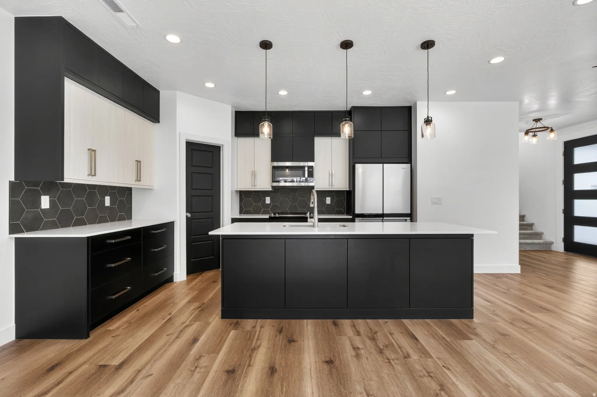 Contemporary kitchen featuring two-tone cabinetry, a central island with a white countertop, recessed lighting, hexagonal backsplash, and wood-finish flooring