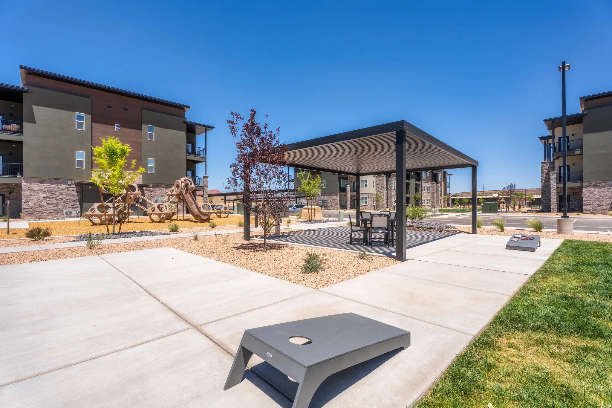 Outdoor amenity area featuring a modern pergola with seating, concrete pathways, and a children's play structure