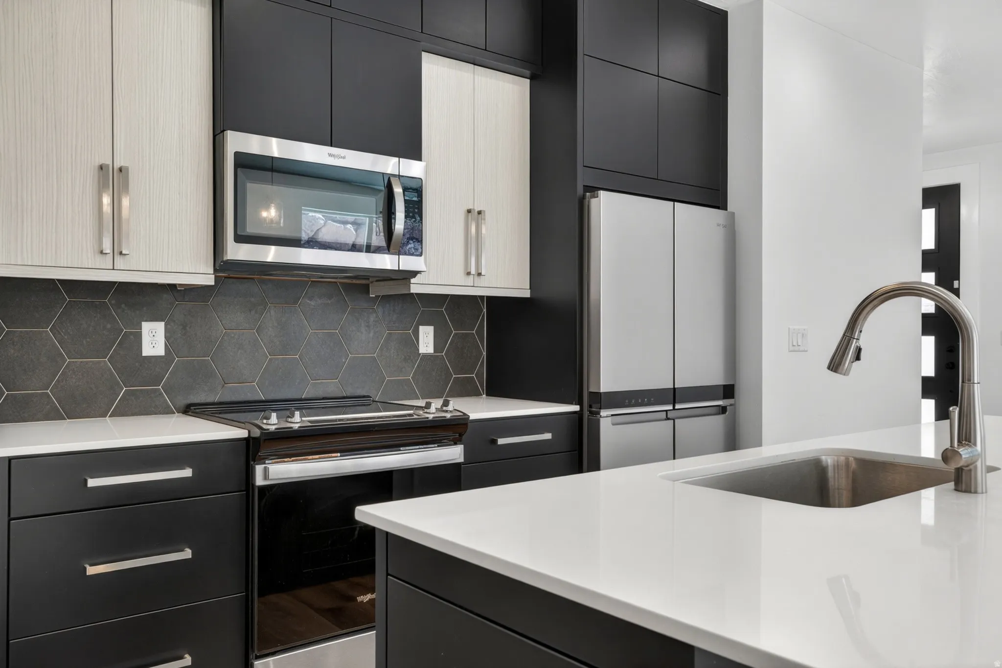 Contemporary kitchen featuring two-tone cabinetry, stainless steel appliances, a hexagonal tile backsplash, white countertops, and an undermount sink with a gooseneck faucet