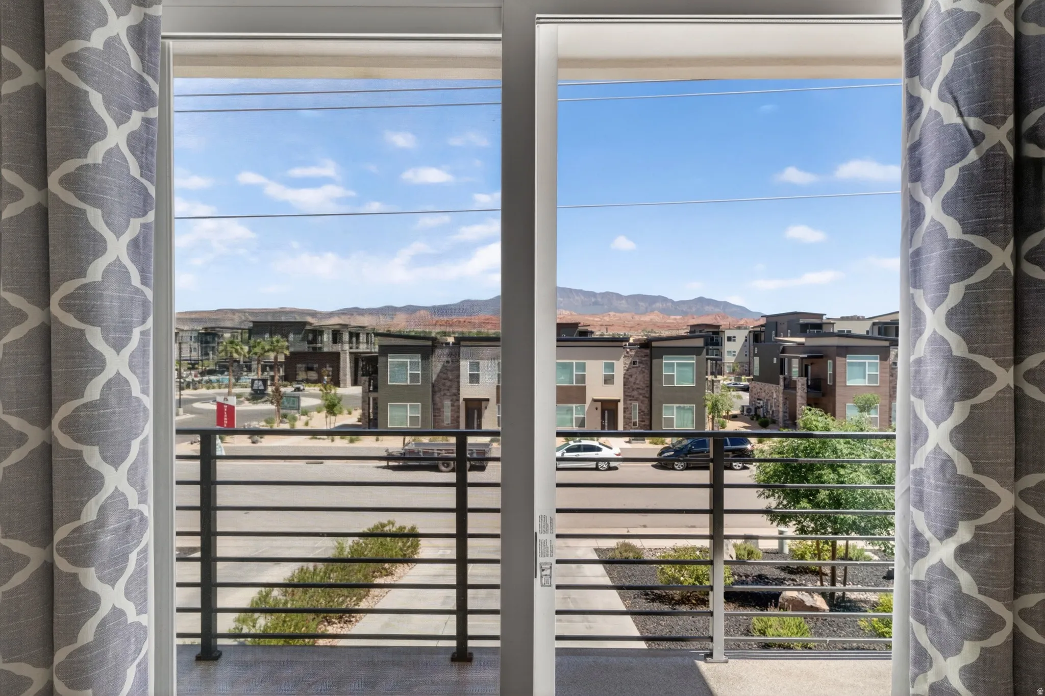 Private balcony with black horizontal bar railing, offering exterior views of contemporary architecture, desert landscaping, and distant red rock formations
