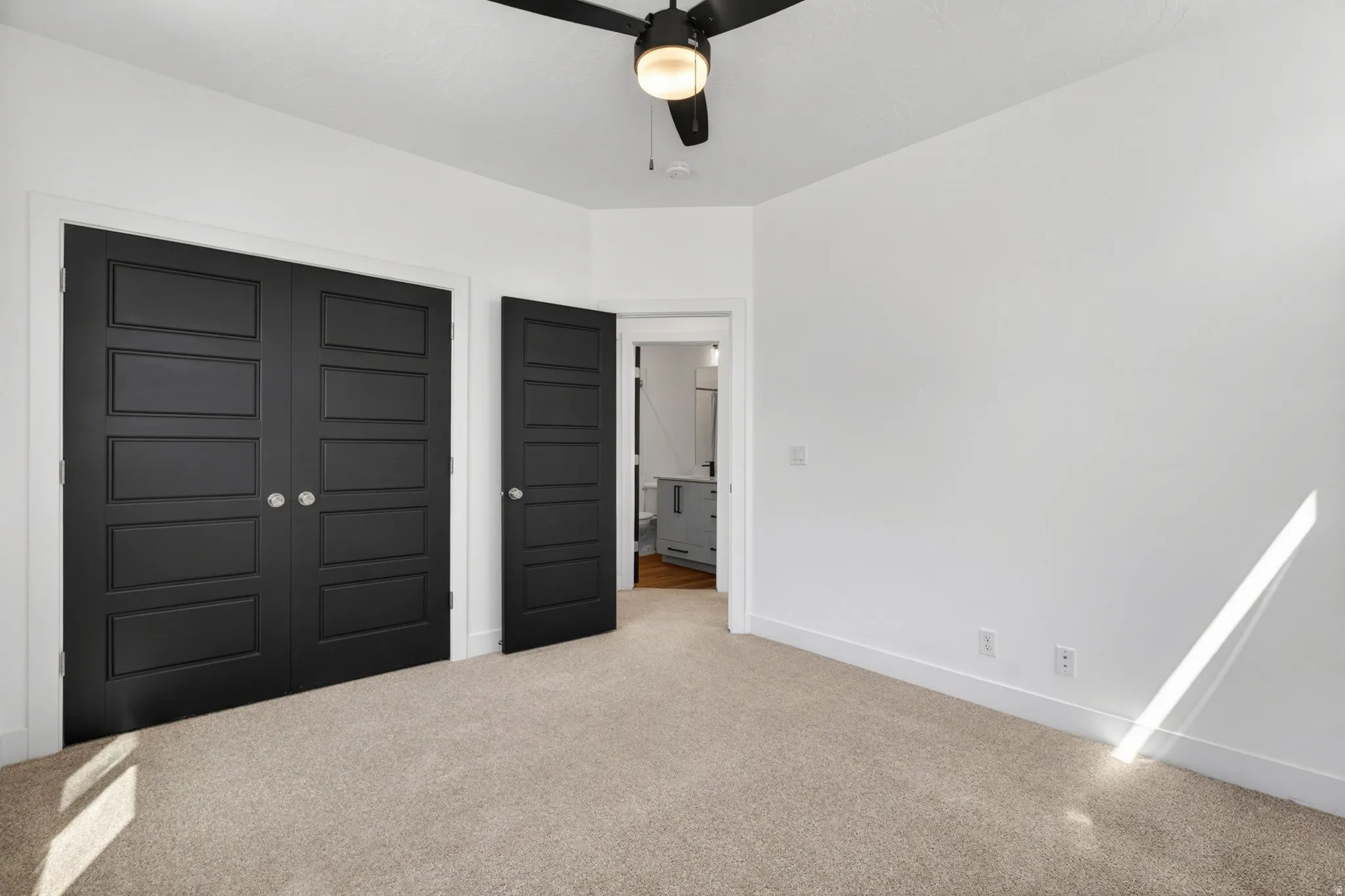 Spacious room featuring neutral carpet flooring, crisp white walls, and a ceiling fan with light fixture
