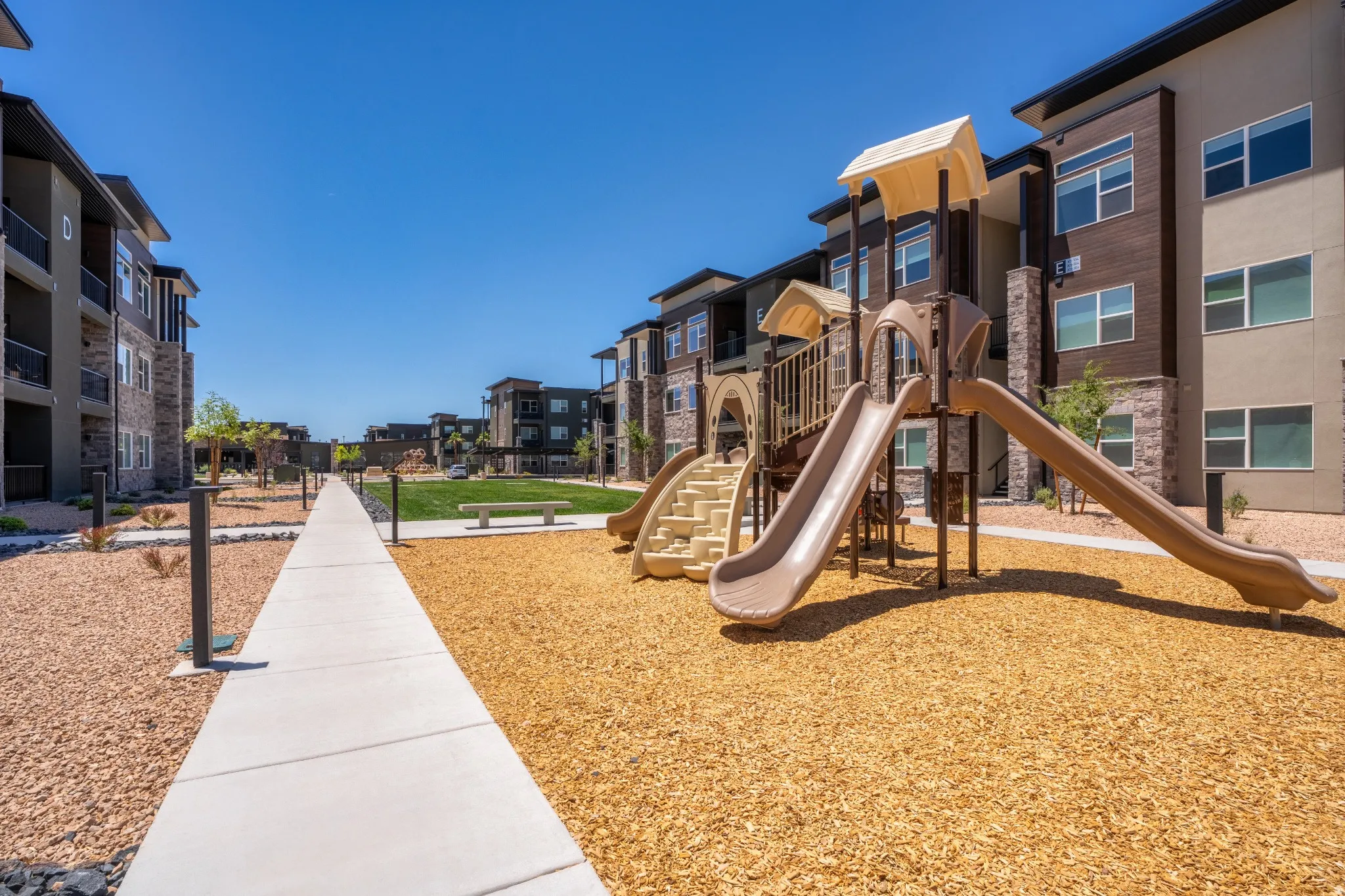 Outdoor playground featuring two slides and a climbing structure, set on a wood chip surface