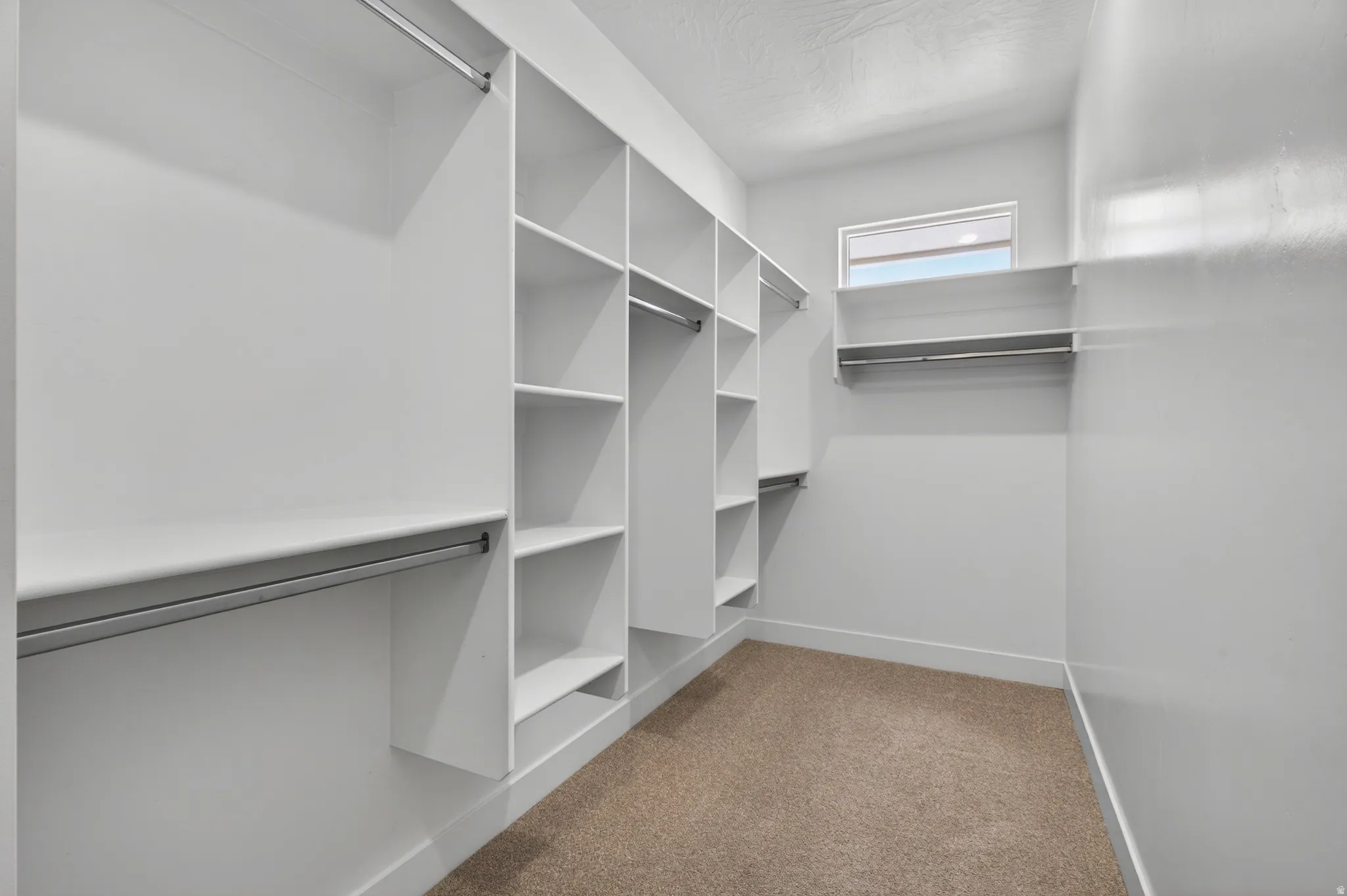 Built-in closet system featuring multiple hanging rods, integrated shelving units, and a window providing natural light