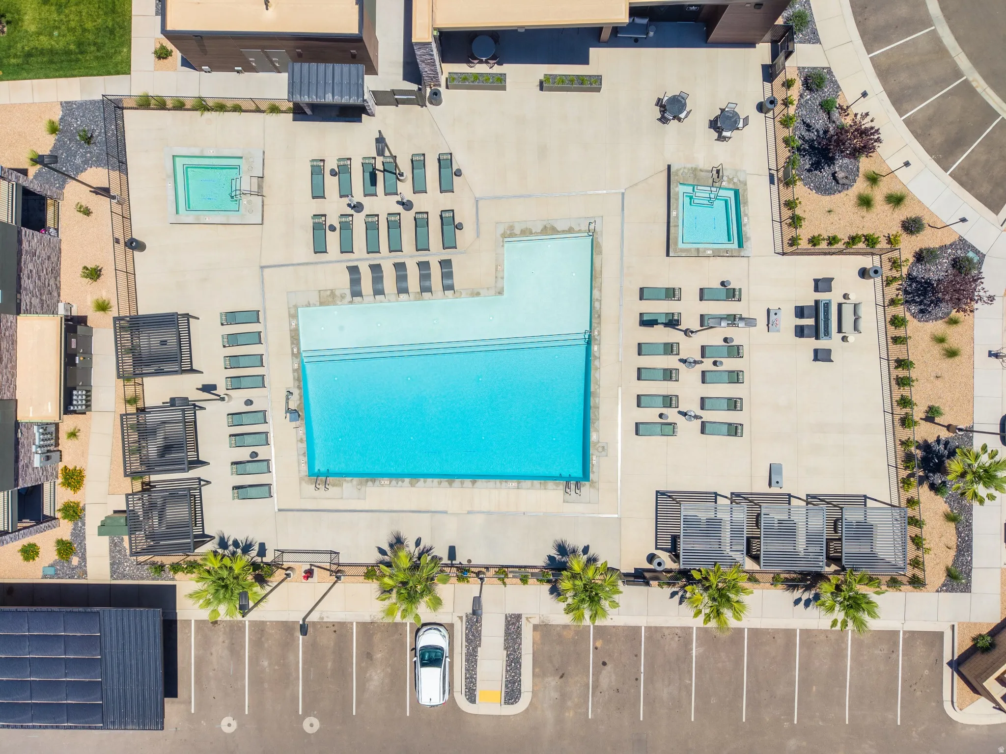 Expansive outdoor amenity area featuring a large swimming pool, two integrated hot tubs, multiple lounge chairs, shaded cabanas, and desert landscaping