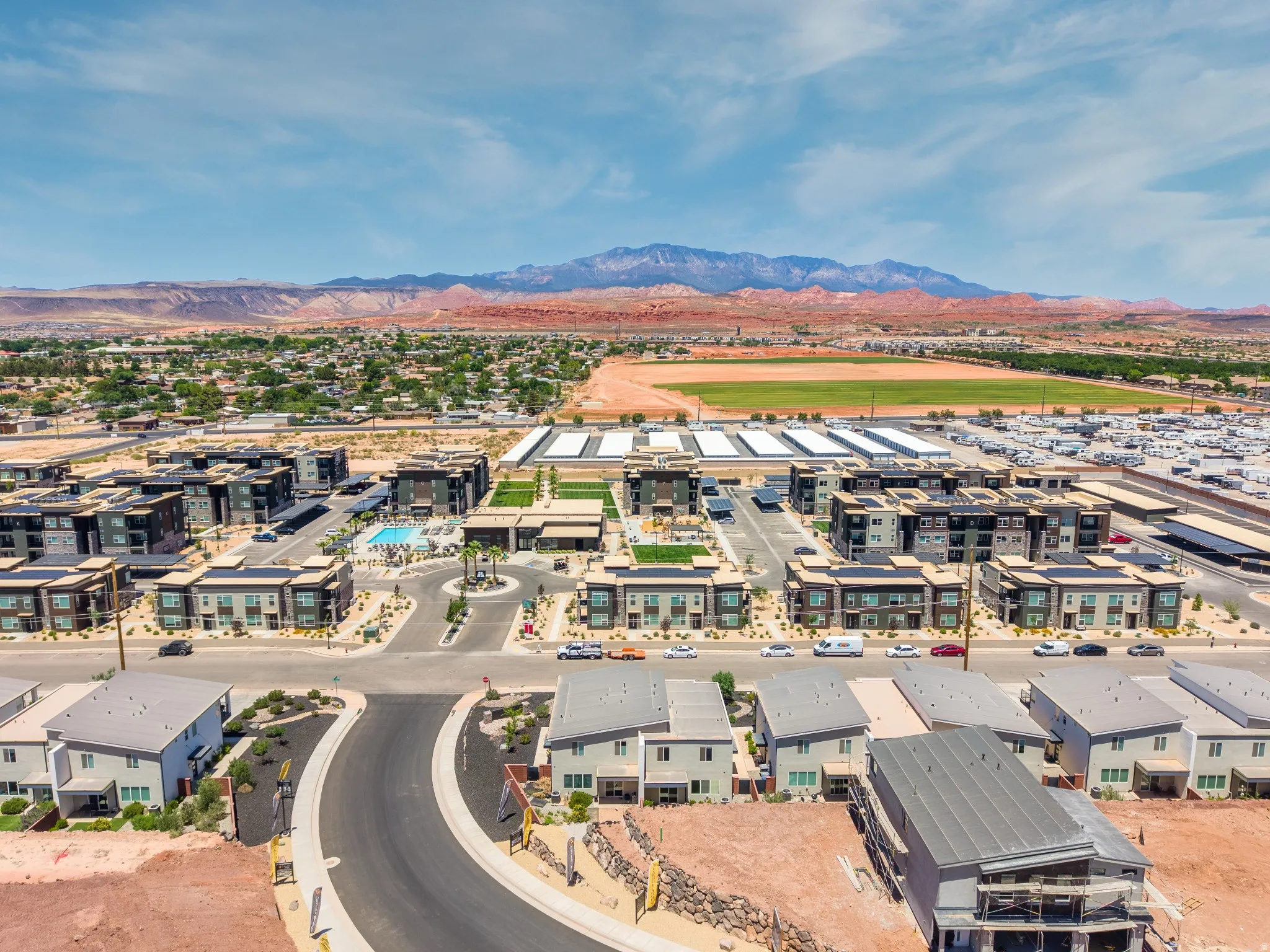Aerial perspective showcasing a community with diverse architectural styles, featuring multi-story residential buildings, a central swimming pool area, and a surrounding landscape of arid terrain and distant mountains