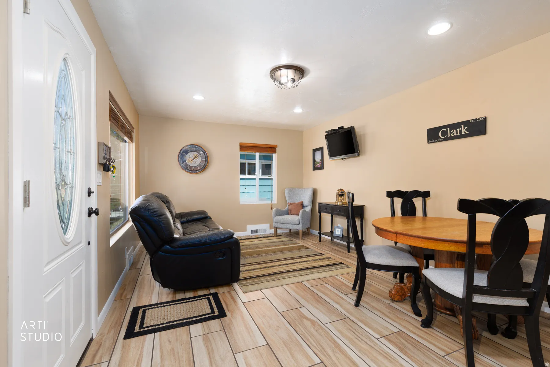 Open-concept living space featuring wood-finish flooring, recessed lighting, and a white entry door with decorative glass