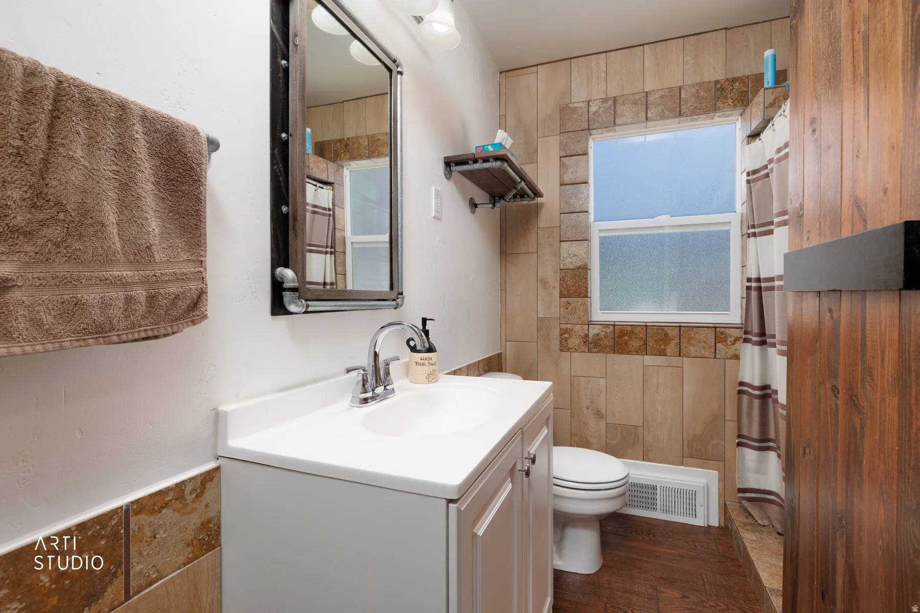 Bathroom featuring a single vanity with a white countertop and chrome faucet, a rectangular mirror with metal frame, a toilet, a window with frosted glass, and wood-finish flooring