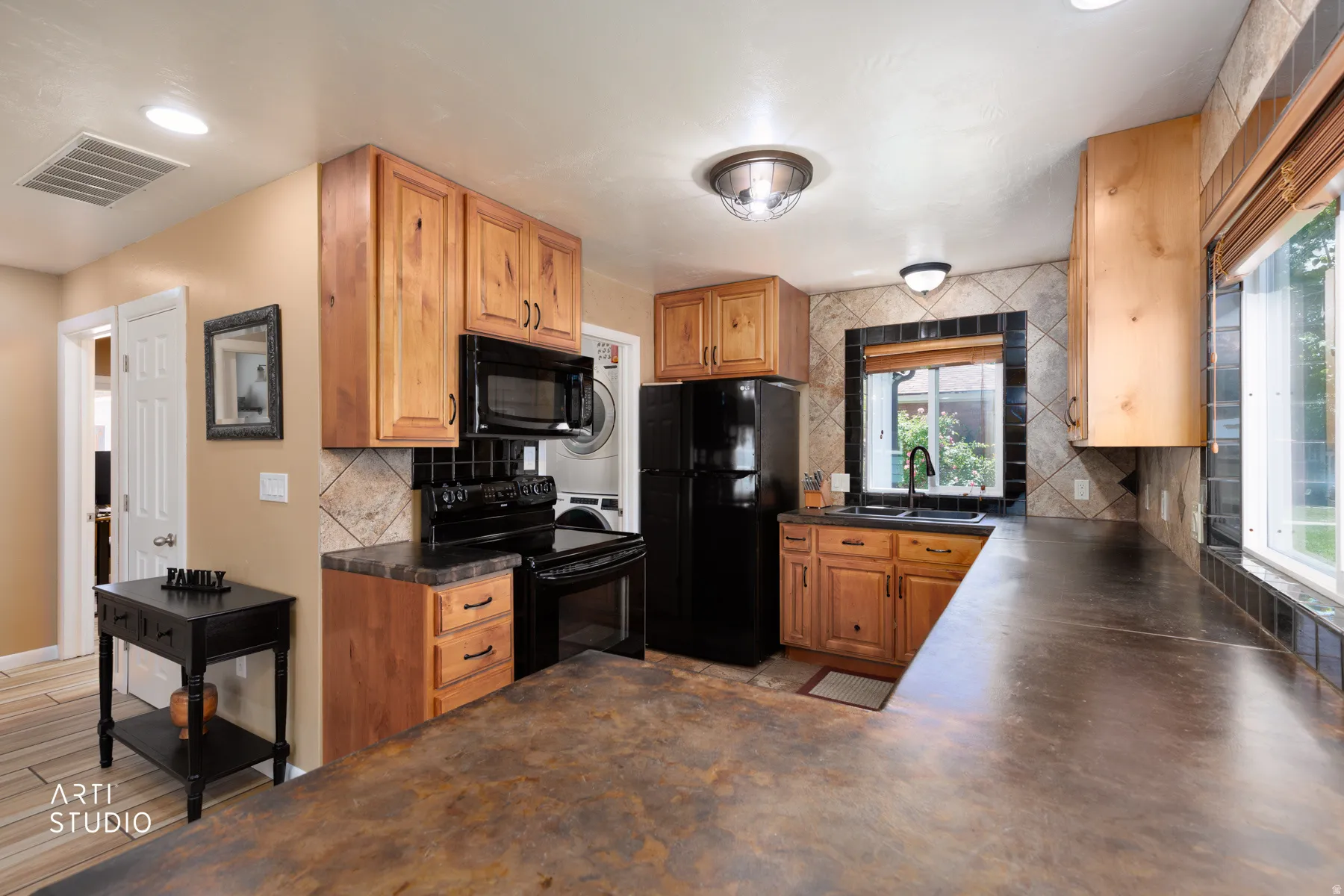 Kitchen featuring wood-finish cabinetry, black appliances, a tile backsplash, and spacious counter surfaces