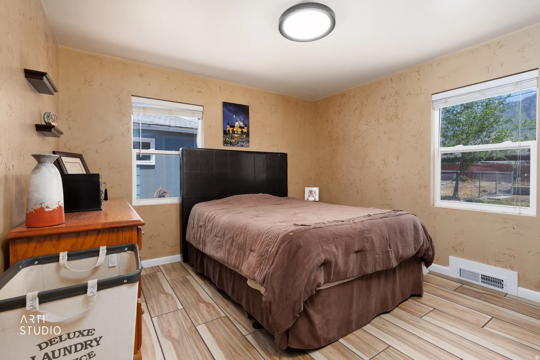 Bedroom featuring textured wall finishes, wood-finish flooring, and two windows providing natural light