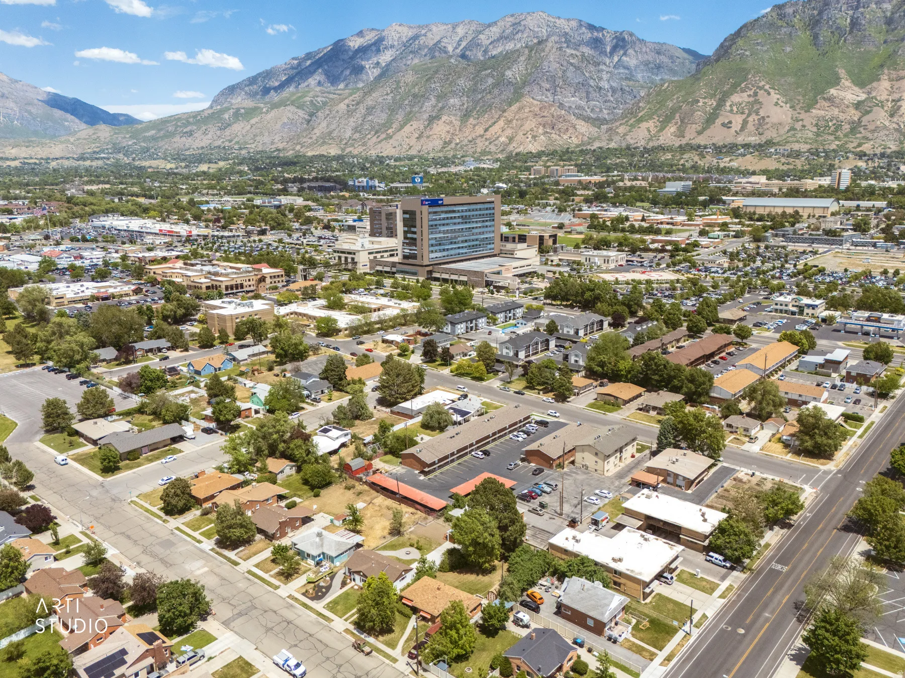 Aerial perspective featuring a mountainous backdrop, urban residential areas, commercial buildings, and mature tree-lined streets