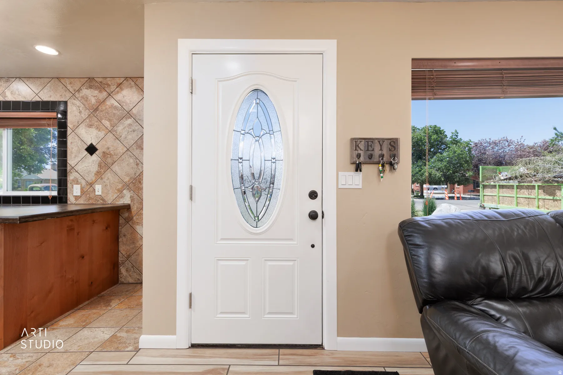 White entry door with decorative oval glass insert, tile flooring, wood-finish cabinetry, and a window with outdoor scenery