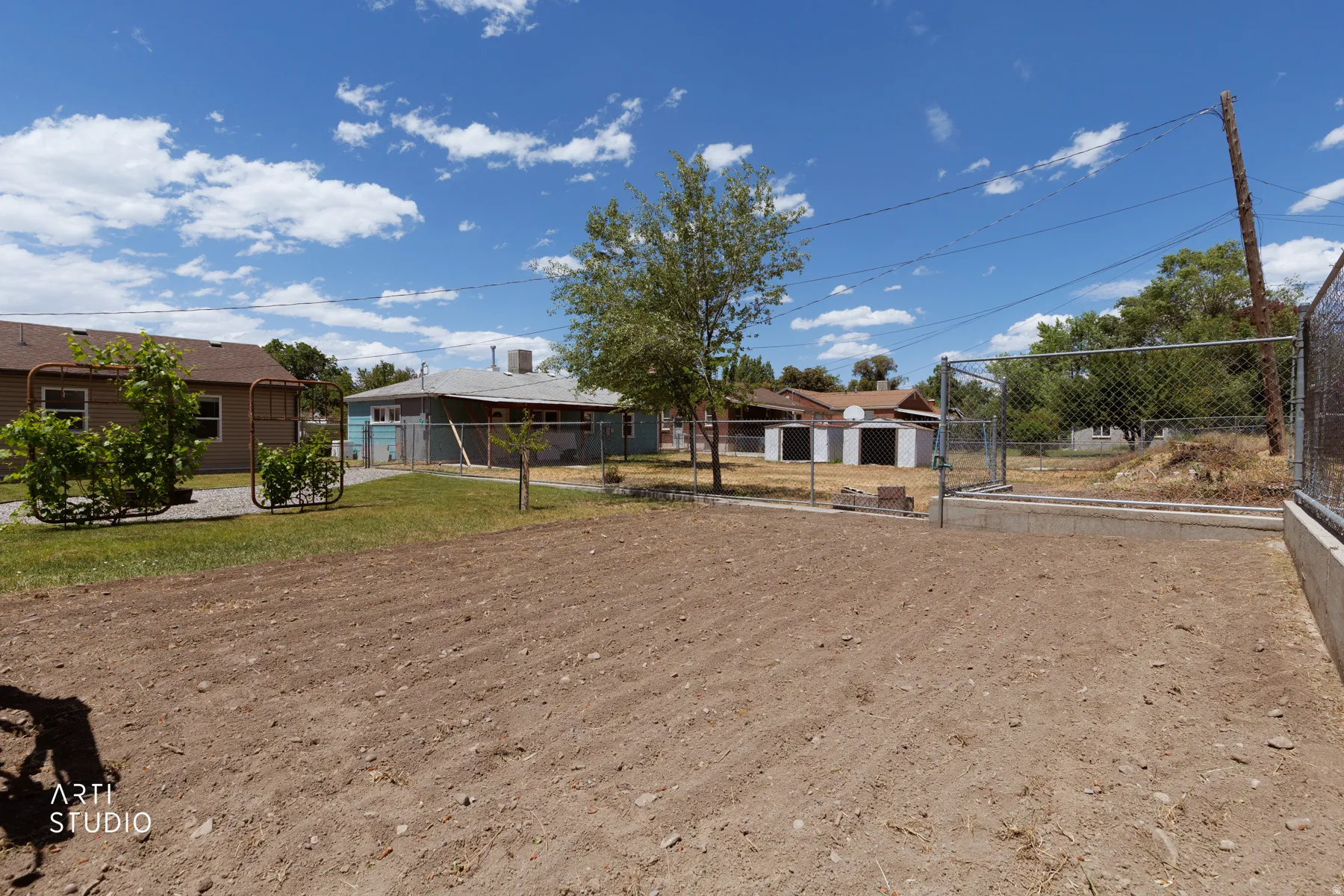 Expansive rear yard with prepared earth, perimeter chain-link fencing, and a concrete retaining wall