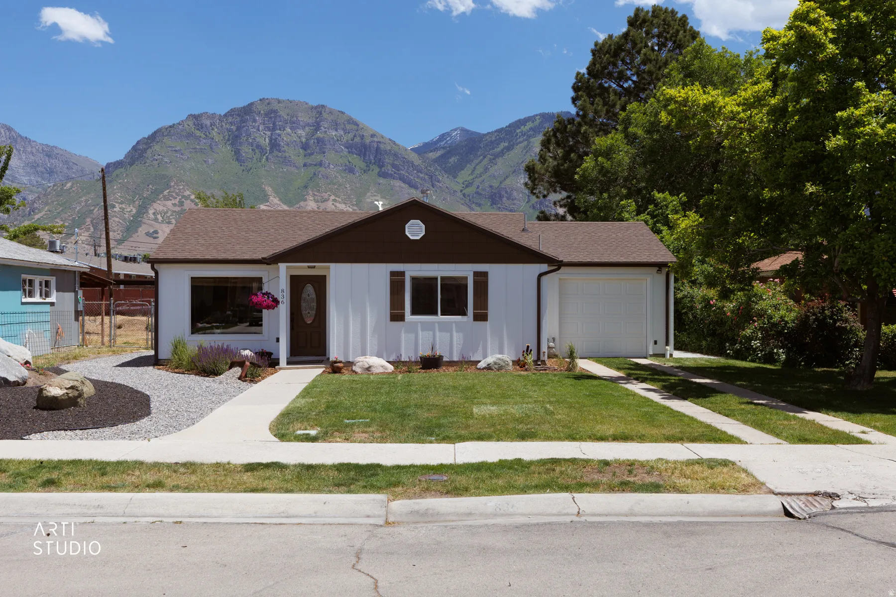Single-story residence featuring white vertical siding, a brown roof, and mountain backdrop