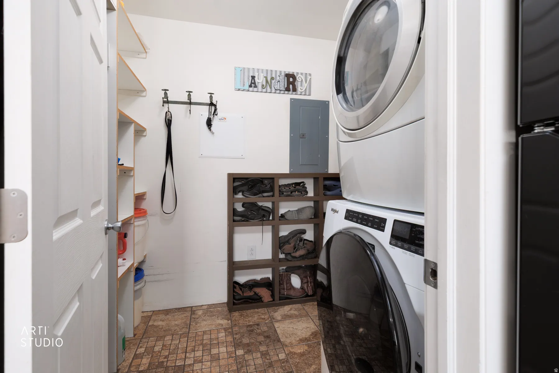 Utility area featuring a stacked washer and dryer unit, built-in shelving, a wall-mounted coat rack, and patterned floor tiles