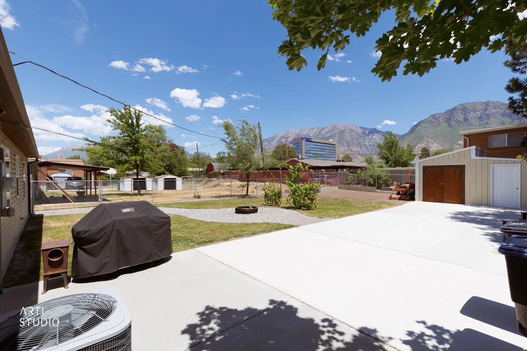 Expansive paved patio area featuring a detached garage with wood-paneled doors, an additional storage shed, and a mountain backdrop