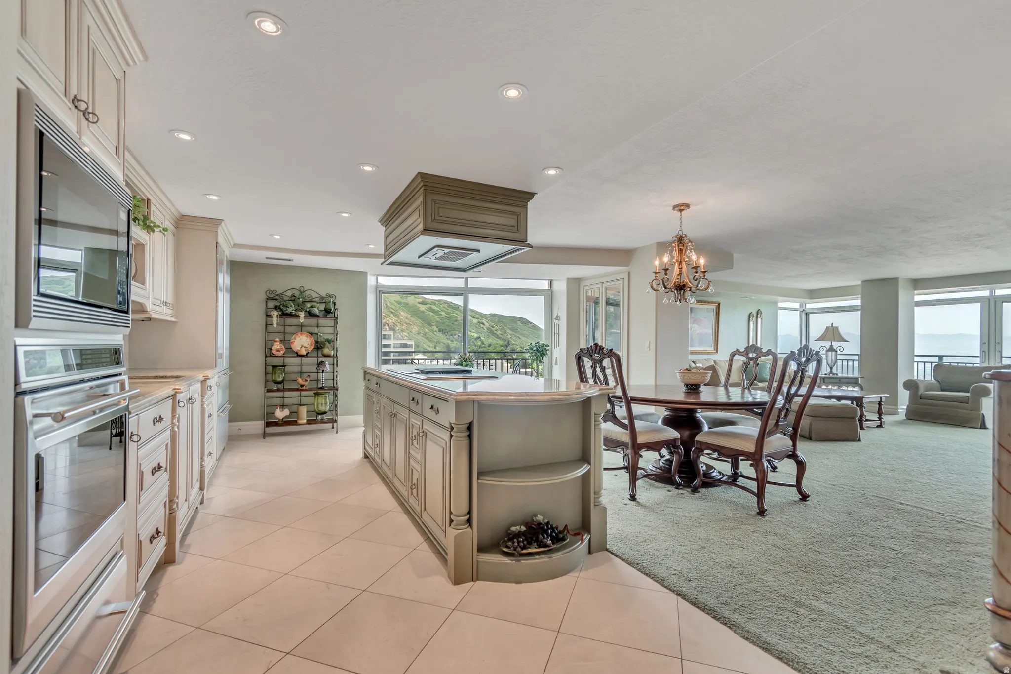 Open-concept kitchen and living area featuring a large center island with integrated range hood, stainless steel built-in oven and microwave, tiled flooring in the kitchen, and expansive views to the north and west